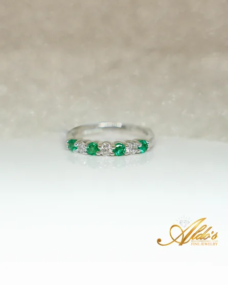 An emerald and diamond band standing upright on a white surface.