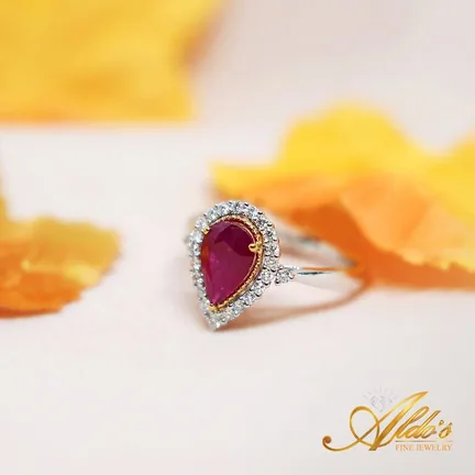 A pear-shaped ruby ring with a diamond halo among orange autumn leaves.
