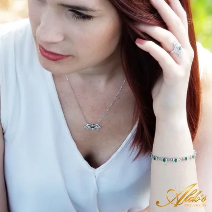 A woman in a white blouse touching her hair, wearing a ring, a pendant and a bracelet.
